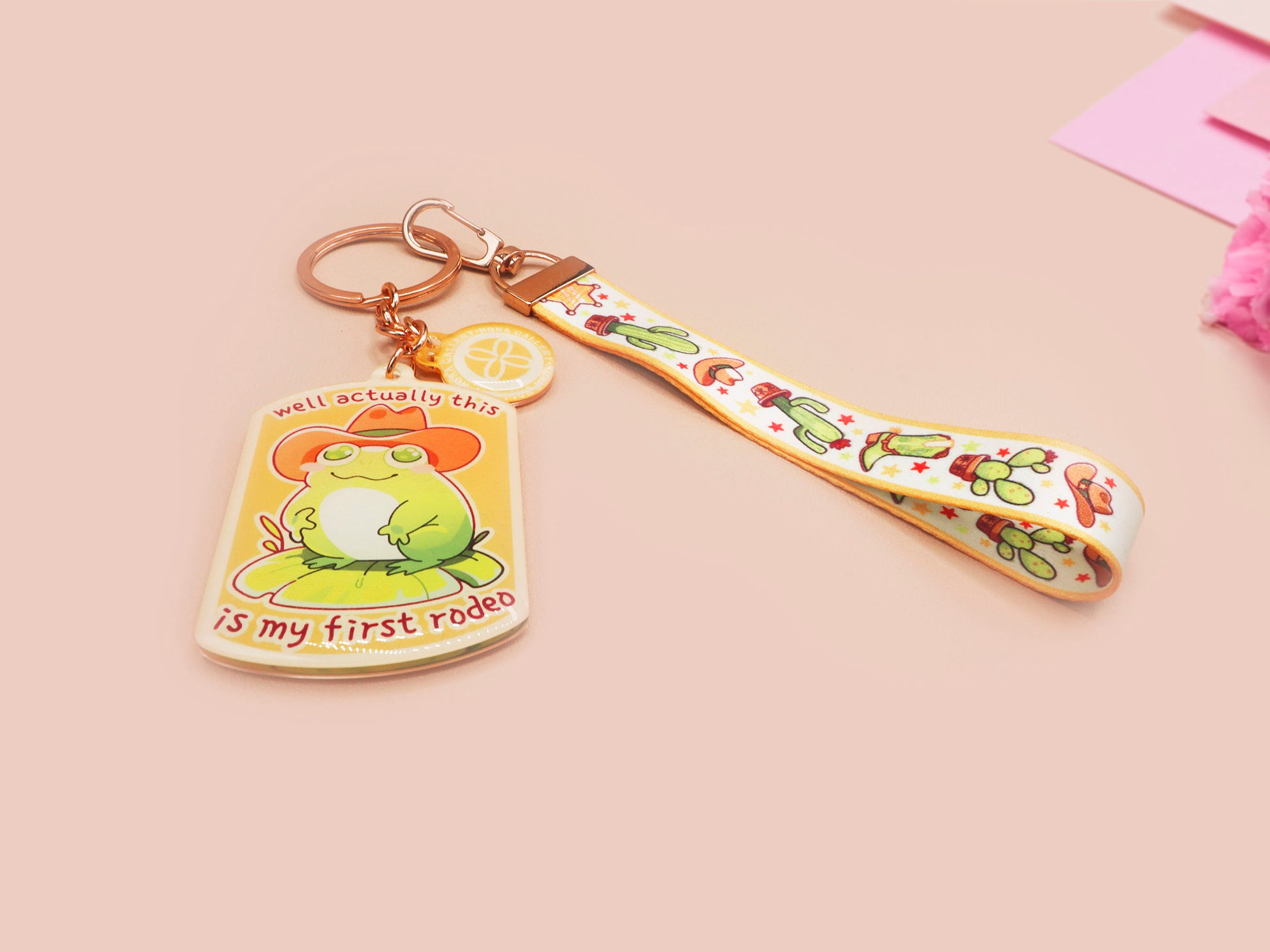 Acrylic keychain and lanyard of a cute cowboy frog with the quote well actually this is my first rodeo With a matching mini sherrif badge charm and lanyard of different country western items like cactus, stetsons and cowboy boots.