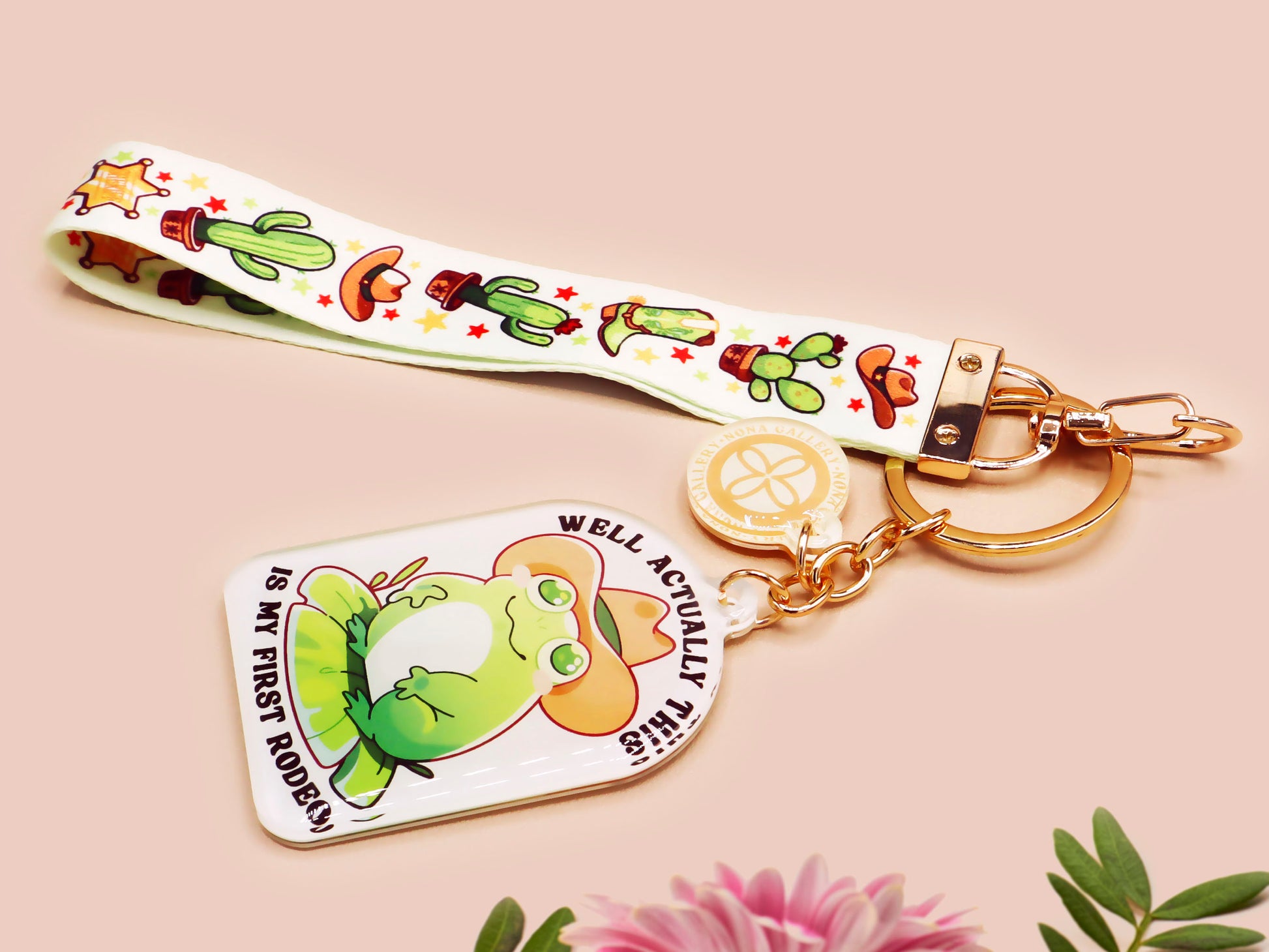 Acrylic epoxy cowboy frog keychain with a large acrylic charm of a cute cowboy frog wearing a stetson hat with the quote well actually this is my first rodeo, a smaller charm of a cute sherrifs badge and a matching cactus and cowboy boots and hats lanyard.
