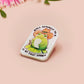 Clear acrylic pin badge with a pink heart-shaped rubber pin back clasp. The design of the pin badge is a cute chibi frog wearing a cowboy hat stetson and the quote well actually this is my first rodeo.