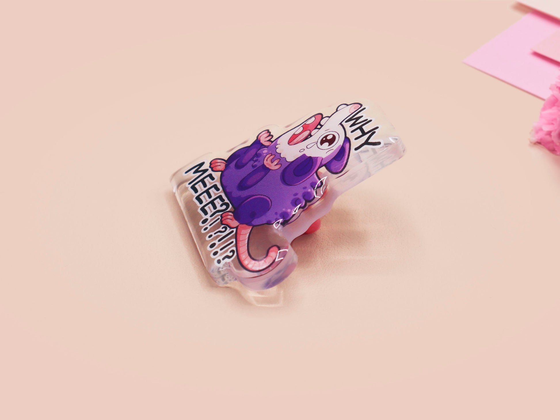 A clear acrylic pin badge with a heart-shaped pin rubber pin back clasp. The design of the pin badge is a cute cartoon screaming possum with the quote why me?!