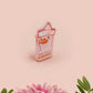 A clear acrylic pin badge with a pink heart-shaped pin back clasp. The design of the pin badge is of a cute chibi goose wearing a paper hat with the quote you silly goose.