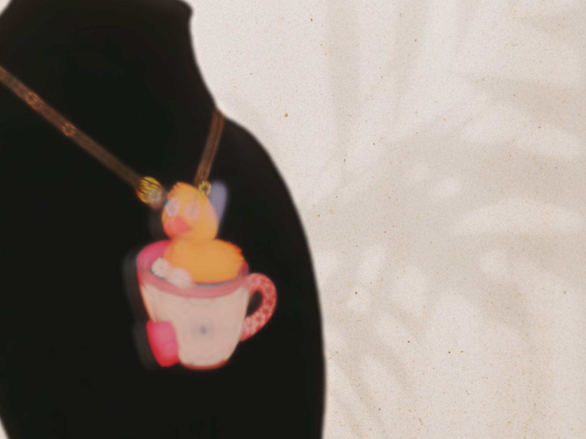 Video of the front and back of a mixed material handmade necklace of chibi cartoon duck sat in a pearlescent witch's brew teacup, with a gold chain and black gift box with a yellow familiars collection gift sleeve on black bust