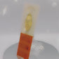 Video of the front and back of the Gold Enamel Talisman Pin with yellow design and the words Artist's Talisman sits on a long white and orange backing card with gold accents. The backing card has details the symbolism of the different design elements of the Talisman pin.