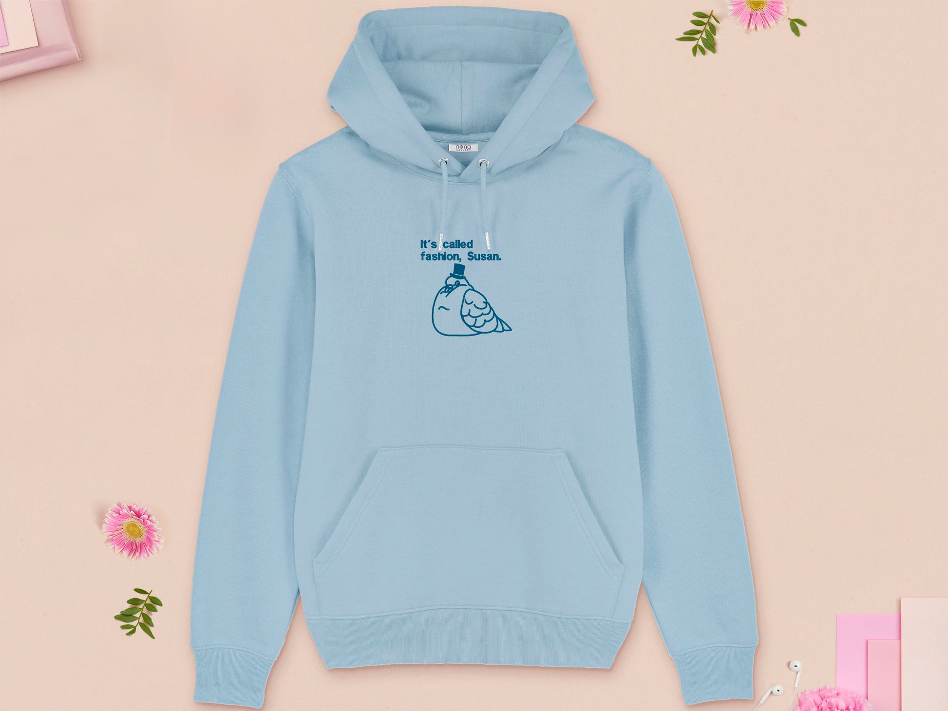 A blue long sleeve fleece hoodie, with an embroidered blue thread design of cute fat pigeon wearing a top hat with text underneath reading It's Called Fashion, Susan.