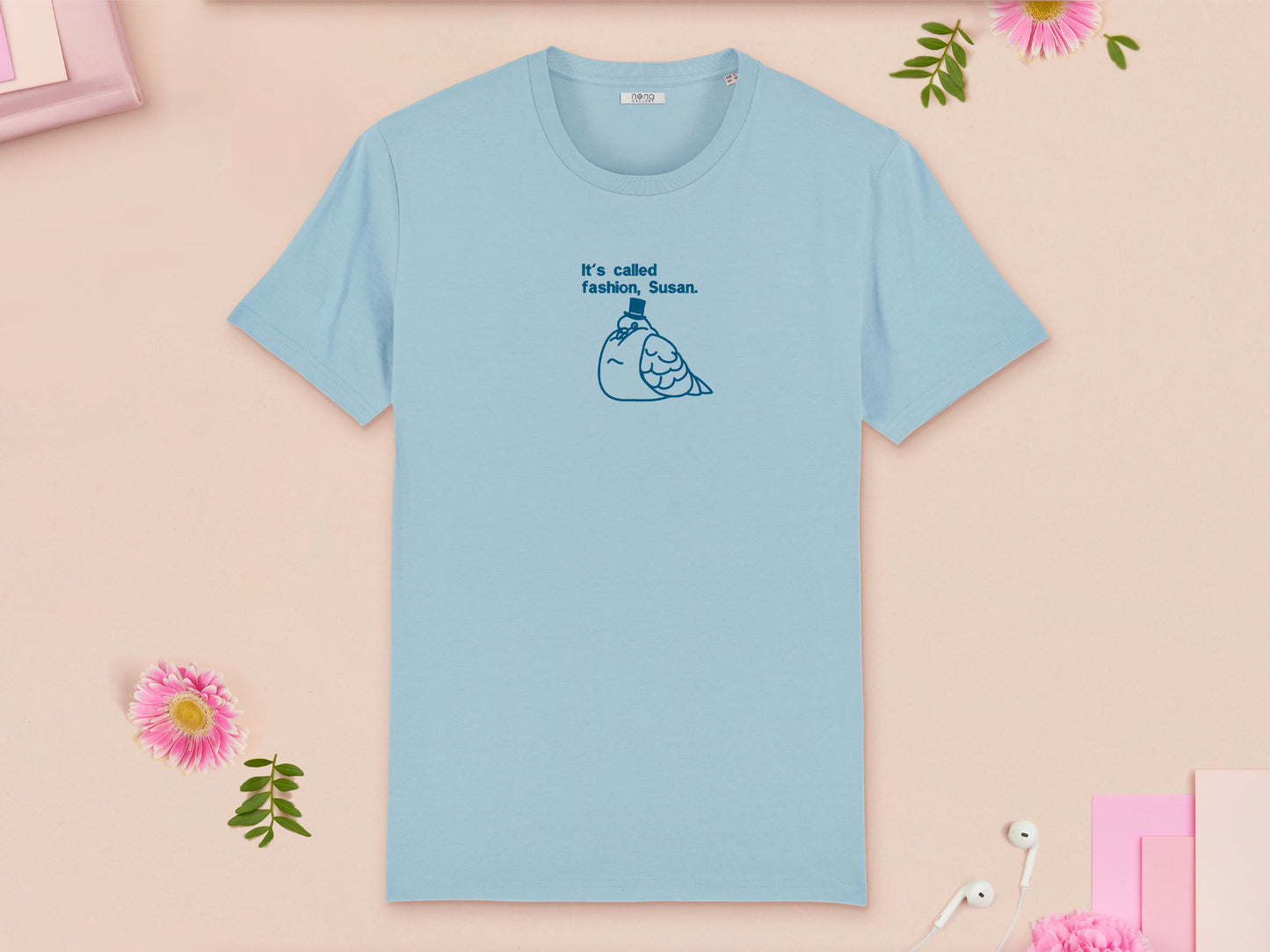 A blue crew neck short sleeve t-shirt, with an embroidered blue thread design of cute fat pigeon wearing a top hat with text underneath reading It's Called Fashion, Susan.