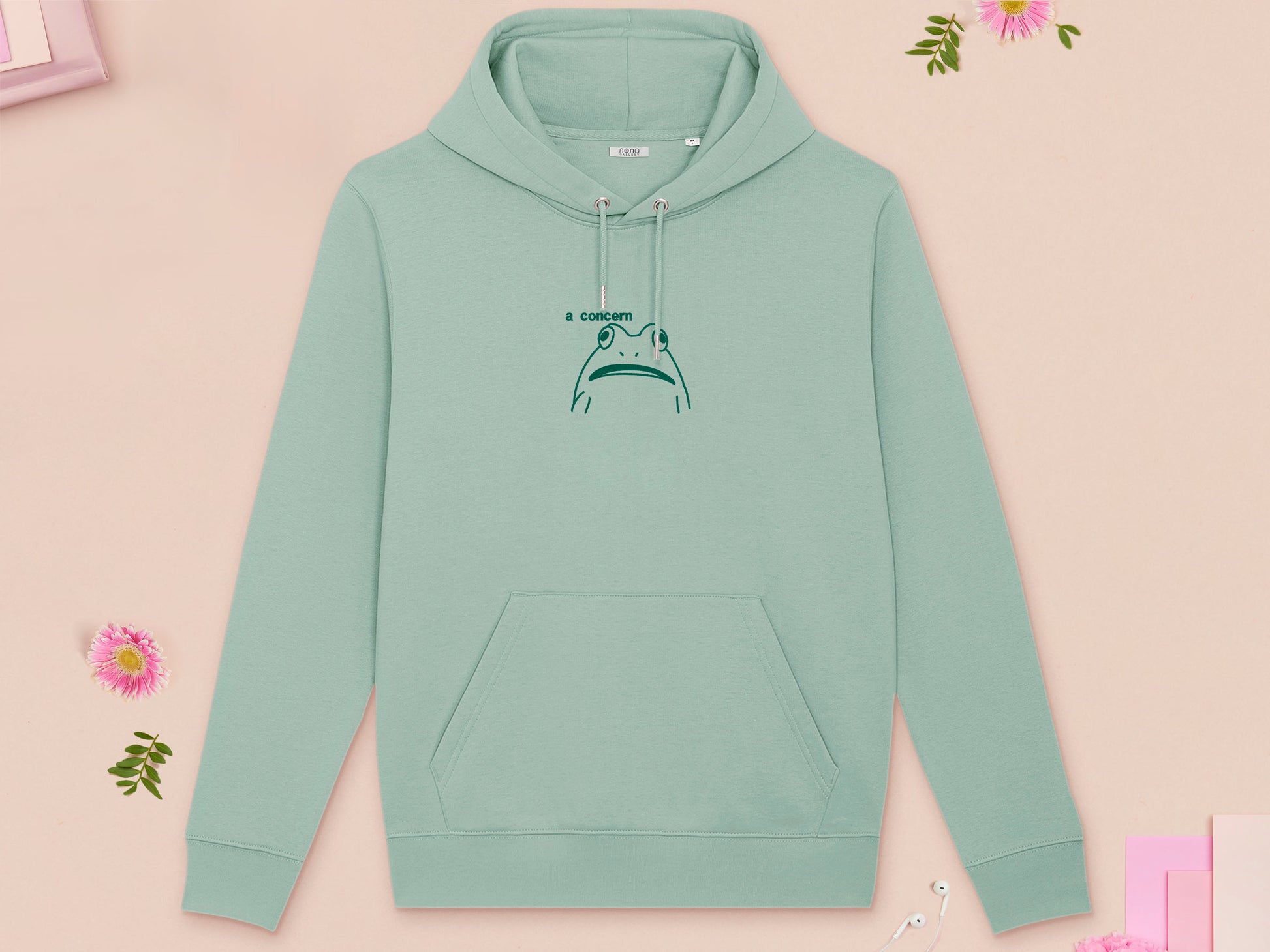 A green long sleeve fleece hoodie, with an embroidered brown thread design of cute confused looking frog with the text a concern.