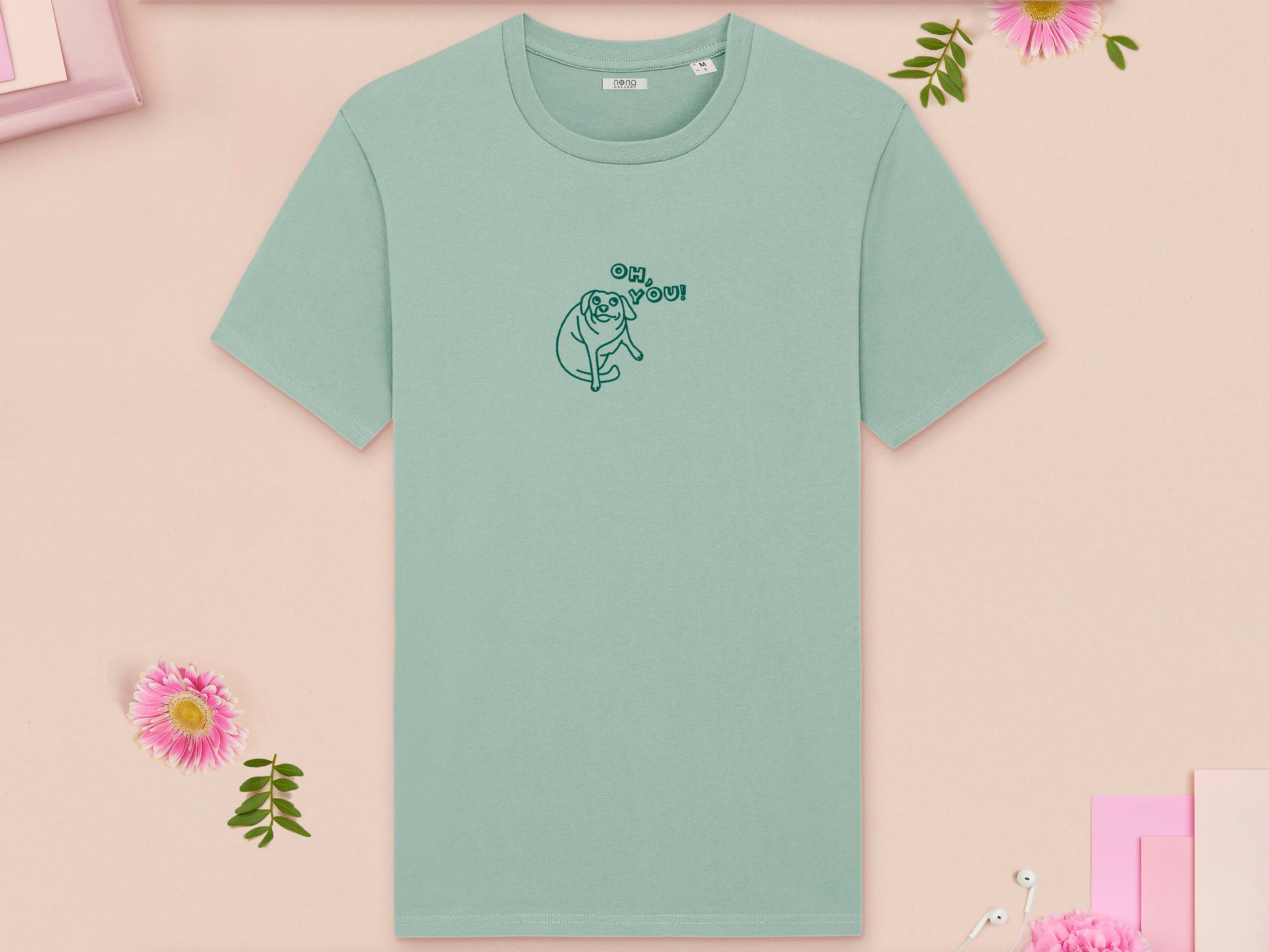 A green crew neck short sleeve t-shirt, with an embroidered green thread design of cute meme dog with cheeky expression and big eyes, with the text Oh You!