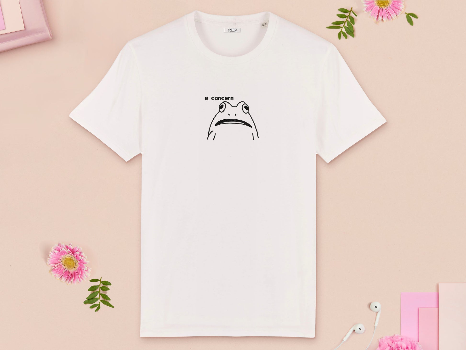 A off white crew neck short sleeve t-shirt, with an embroidered black thread design of cute confused looking frog with the text a concern.