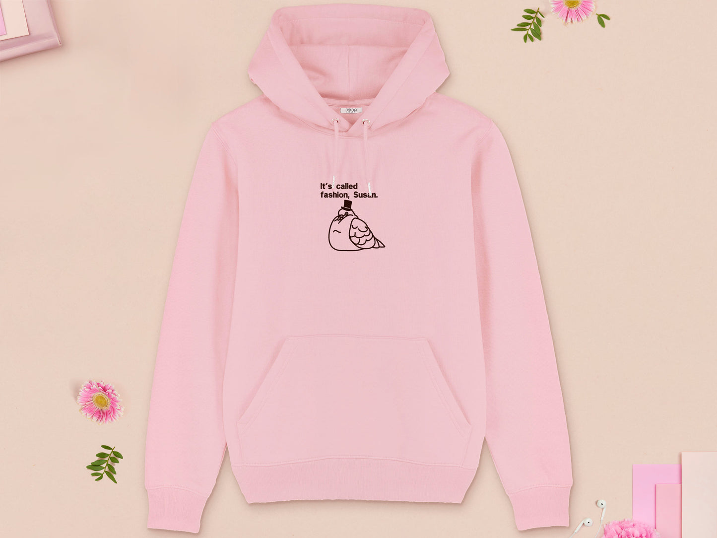 A pink long sleeve fleece hoodie, with an embroidered brown thread design of cute fat pigeon wearing a top hat with text underneath reading It's Called Fashion, Susan.