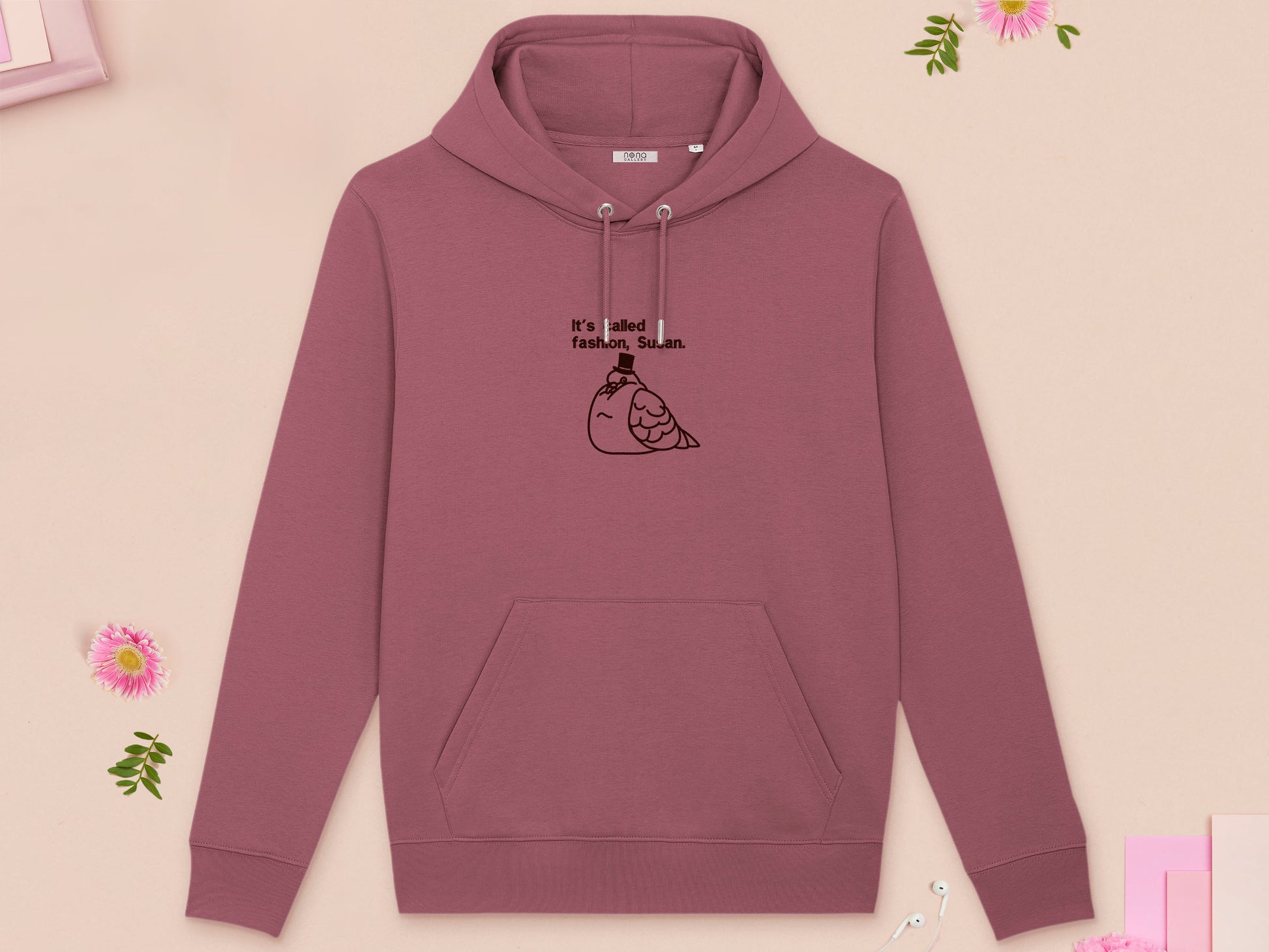 A red long sleeve fleece hoodie, with an embroidered brown thread design of cute fat pigeon wearing a top hat with text underneath reading It's Called Fashion, Susan.