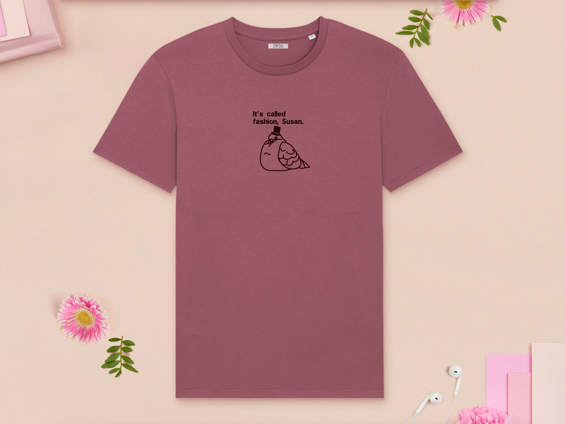 A red crew neck short sleeve t-shirt, with an embroidered brown thread design of cute fat pigeon wearing a top hat with text underneath reading It's Called Fashion, Susan.