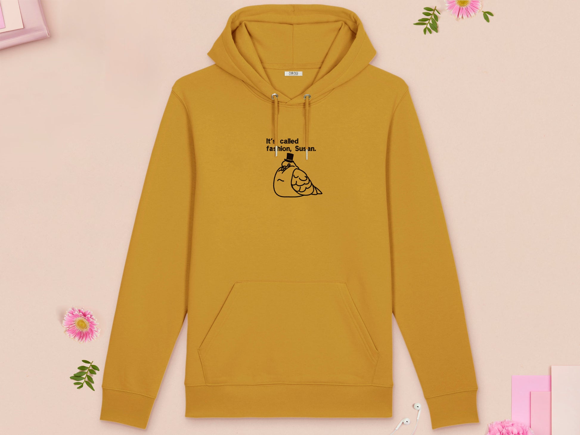 A yellow long sleeve fleece hoodie, with an embroidered black thread design of cute fat pigeon wearing a top hat with text underneath reading It's Called Fashion, Susan.