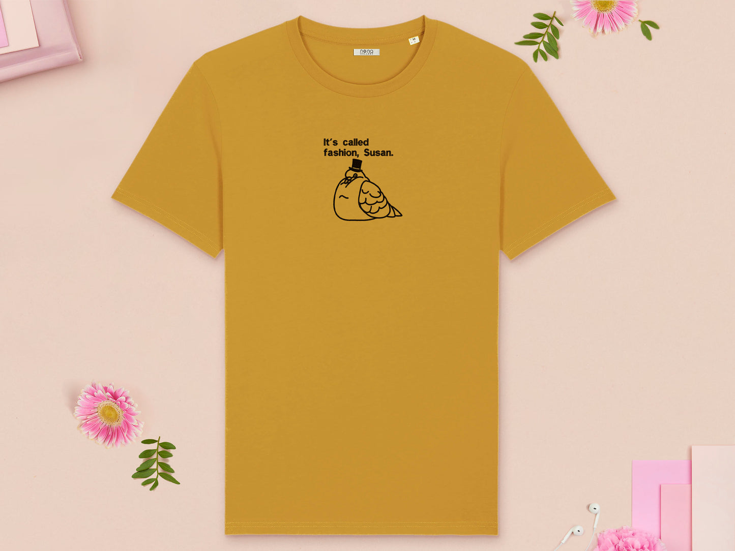 A yellow crew neck short sleeve t-shirt, with an embroidered black thread design of cute fat pigeon wearing a top hat with text underneath reading It's Called Fashion, Susan.